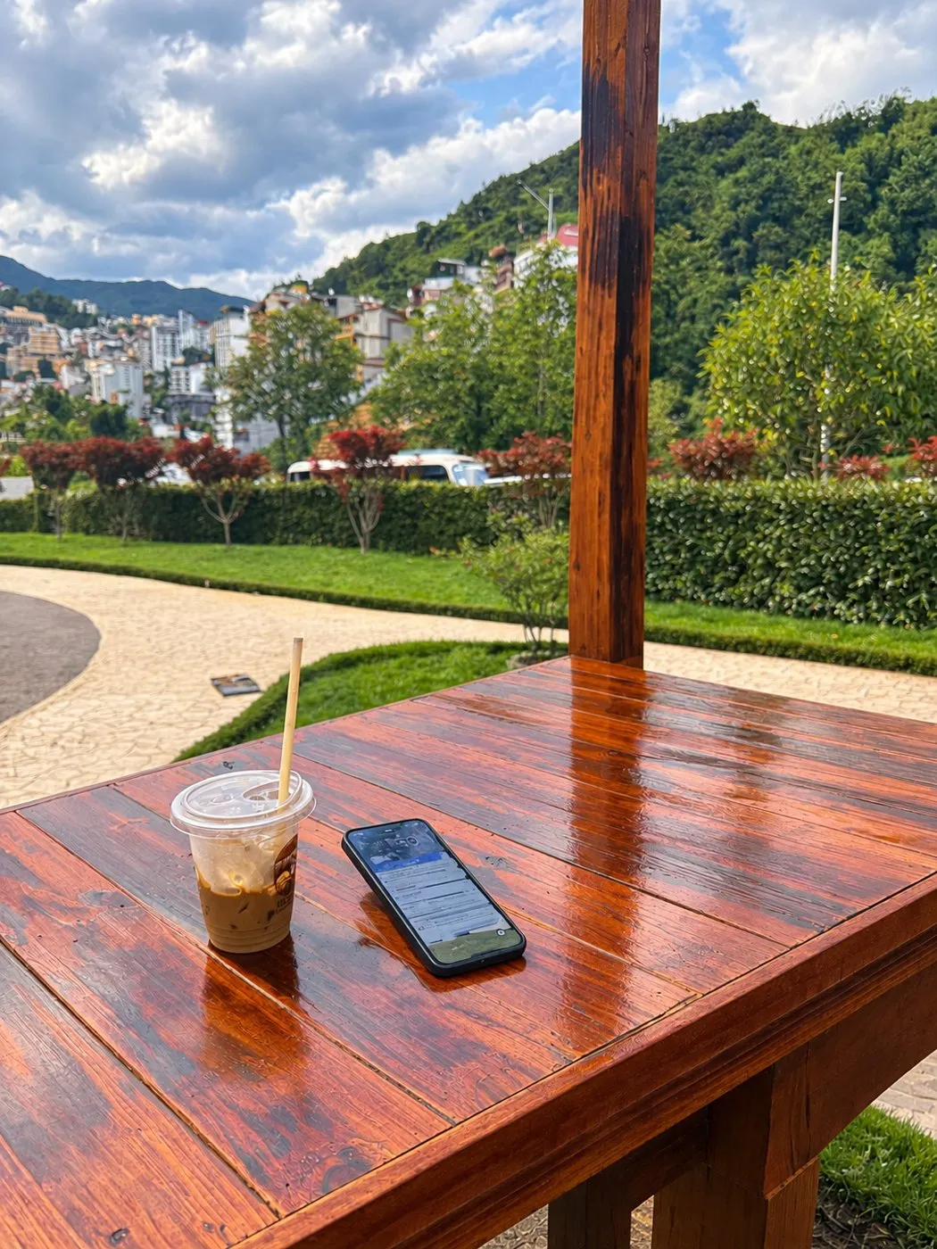 Iced coffee and a phone on a wooden café table with hills behind
